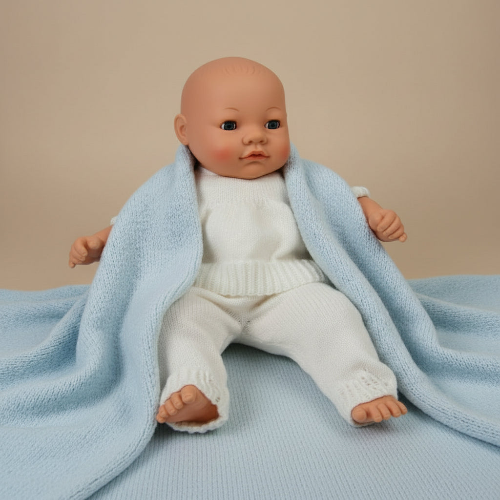 Baby doll wearing a white knitted outfit on a neutral background.
