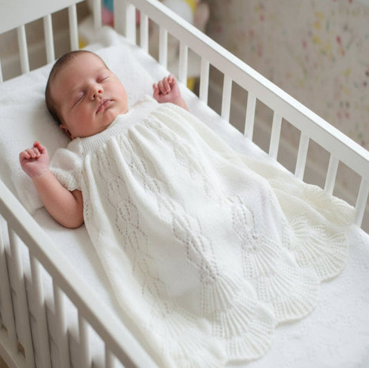 White knitted baby christening gown on a baby laying in a crib on a neutral background