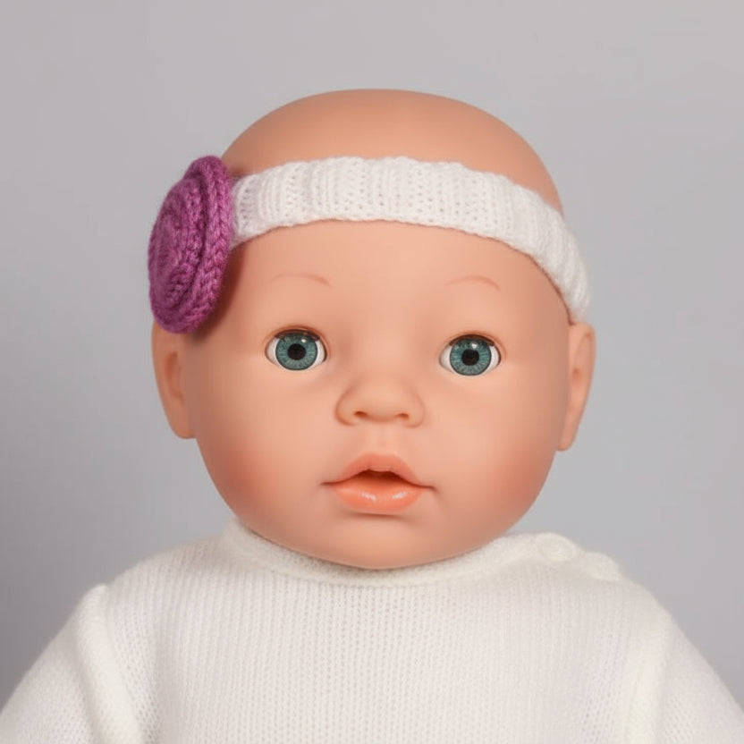 Close-up of a doll head with a white headband and purple circle on a wooden surface.